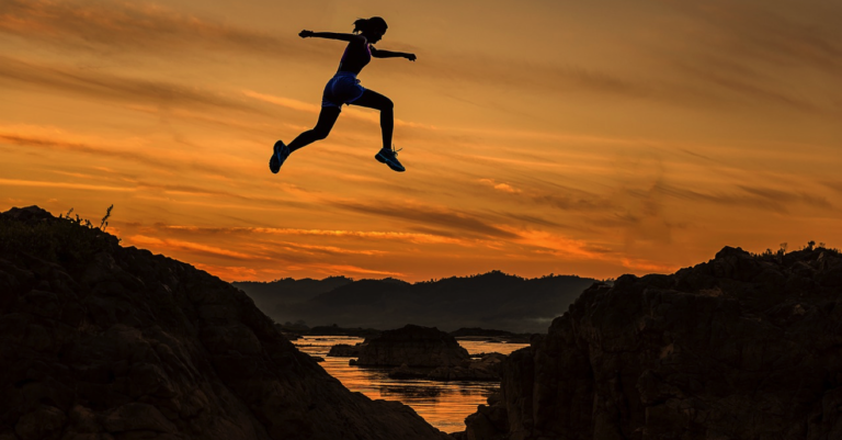 woman jumping between cliffs