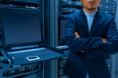 man in suite with arms crossed standing on front of a terminal in a server room