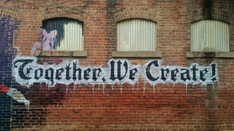 the words together, we create! written as graffiti on a brick wall