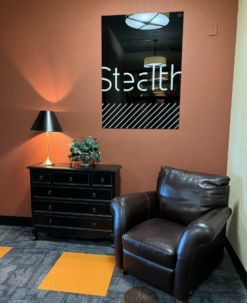a comfortable chair in the corner of the Joplin office with the Stealth sign behind it