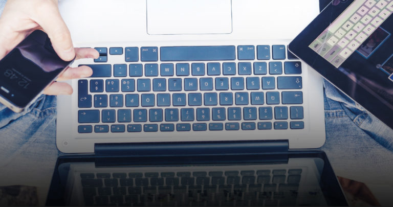 hands holding a phone and tablet over a laptop keyboard