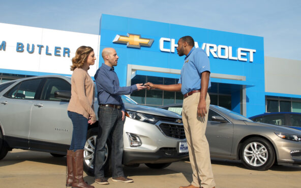 a jim butler sales associate handing over keys to a couple in front of their new car