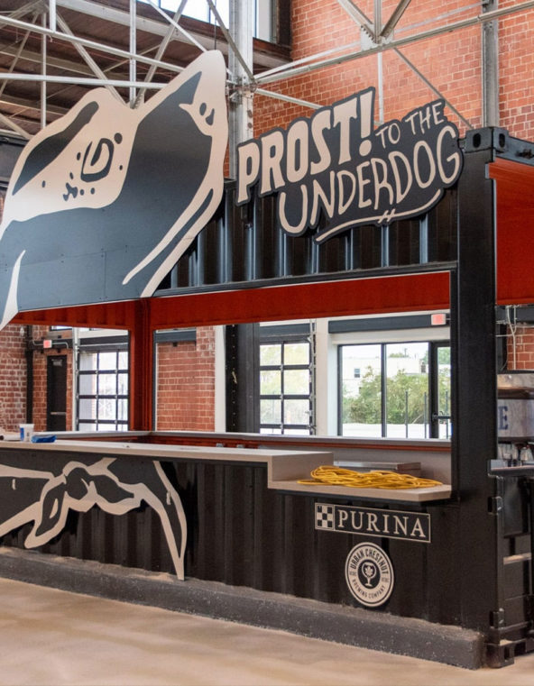 construction image of a shipping container turned into a bar with a cutout of a dog on it and the words prost to the underdog